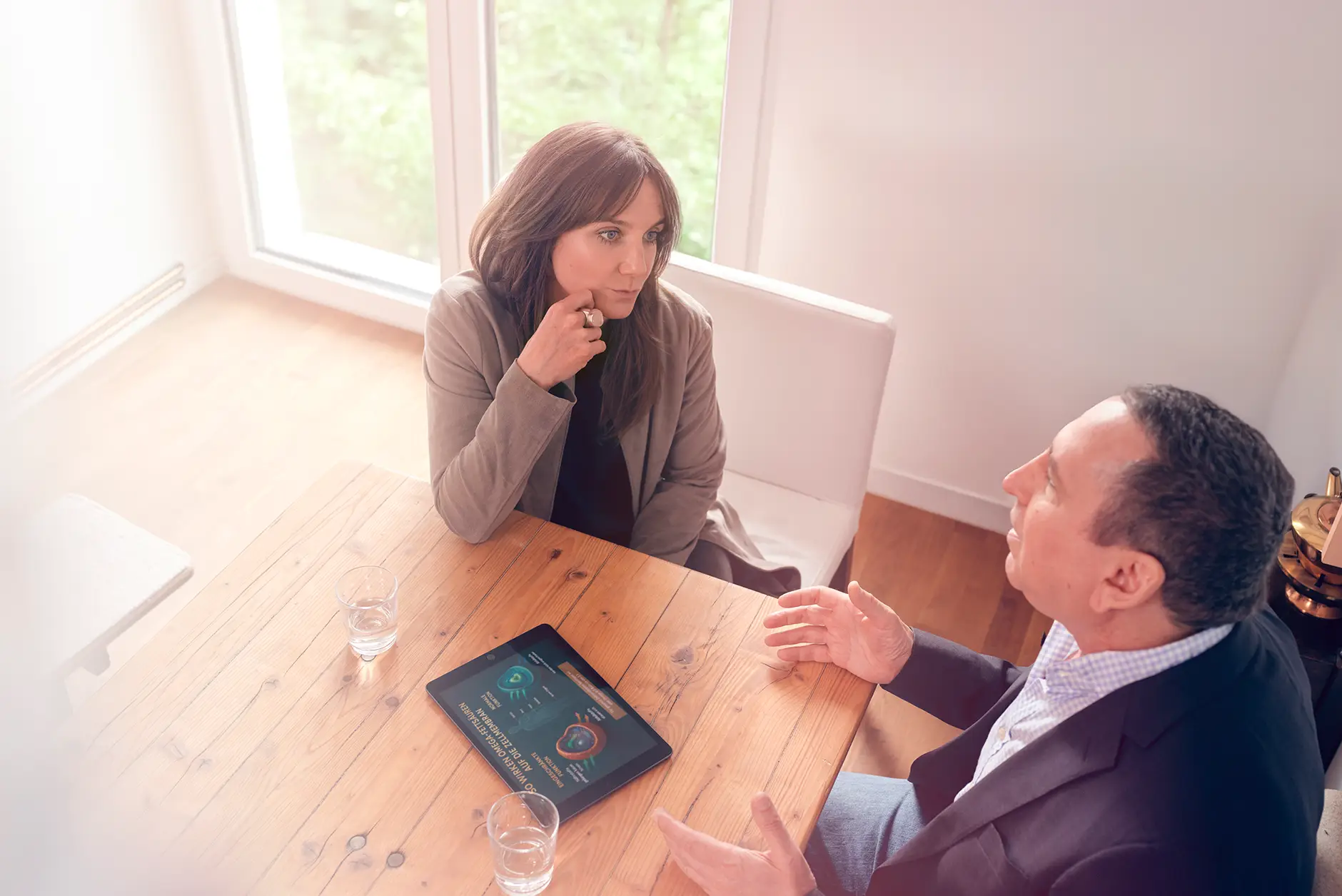 Janna Raphaela Odesser führt ein intensives Gespräch mit einem Patienten an einem Holztisch, auf dem ein Tablet mit grafischen Darstellungen liegt – fokussierte psychologische Arbeit in heller, ruhiger Umgebung