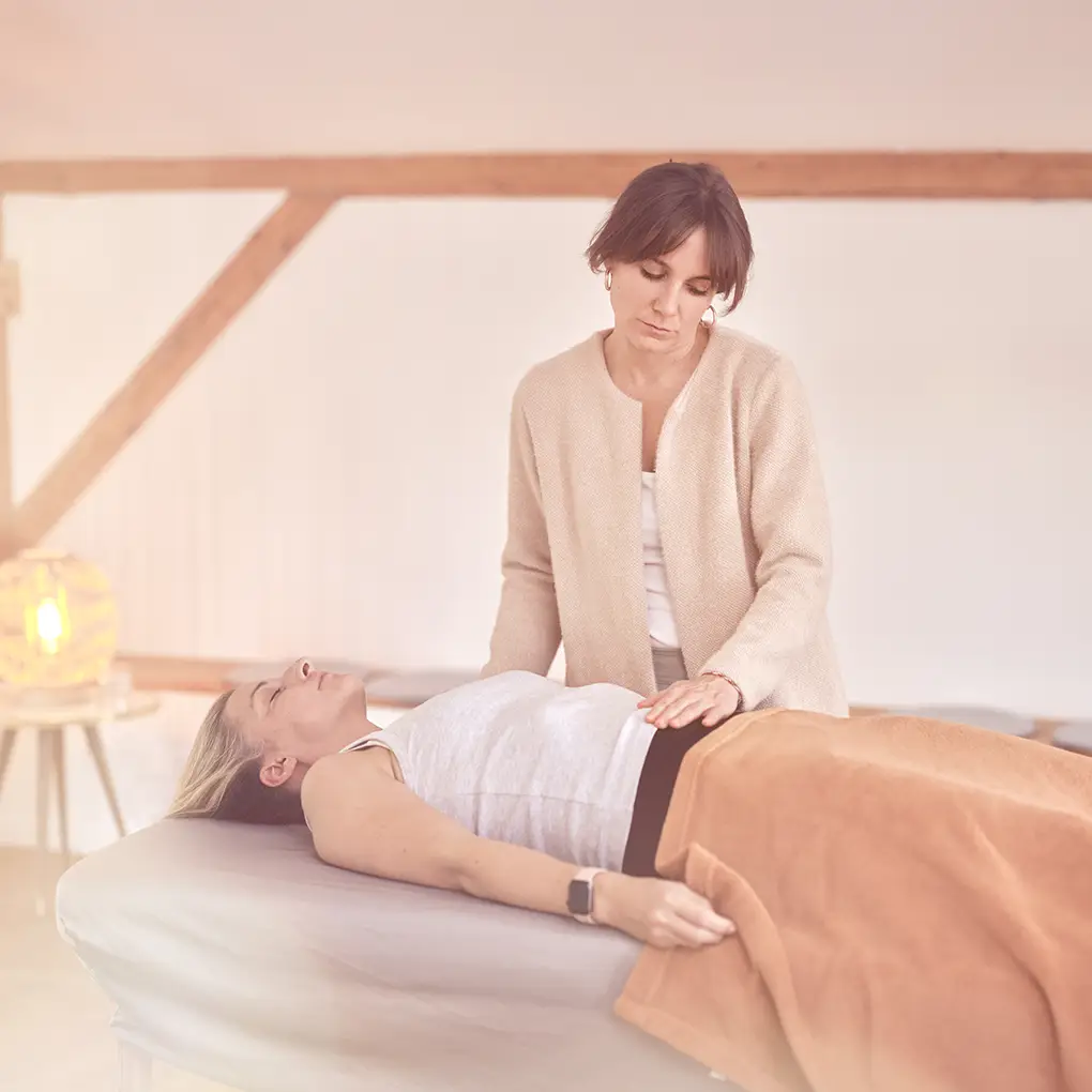 Janna Raphaela Odesser legt beruhigend die Hände auf den Bauch einer liegenden Person während einer Behandlung